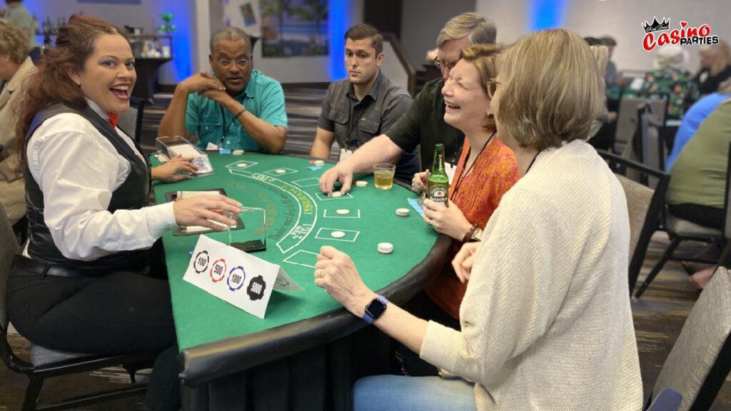 An expressive female casino dealer hosting a blackjack game for adult and senior guests at a luxury 60th birthday casino party theme event.