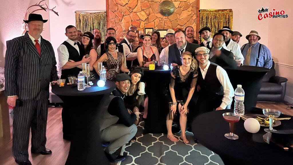 Guests in Roaring 20s flapper and tuxedo costumes playing at a professional blackjack table during a 60th birthday Gatsby casino party.